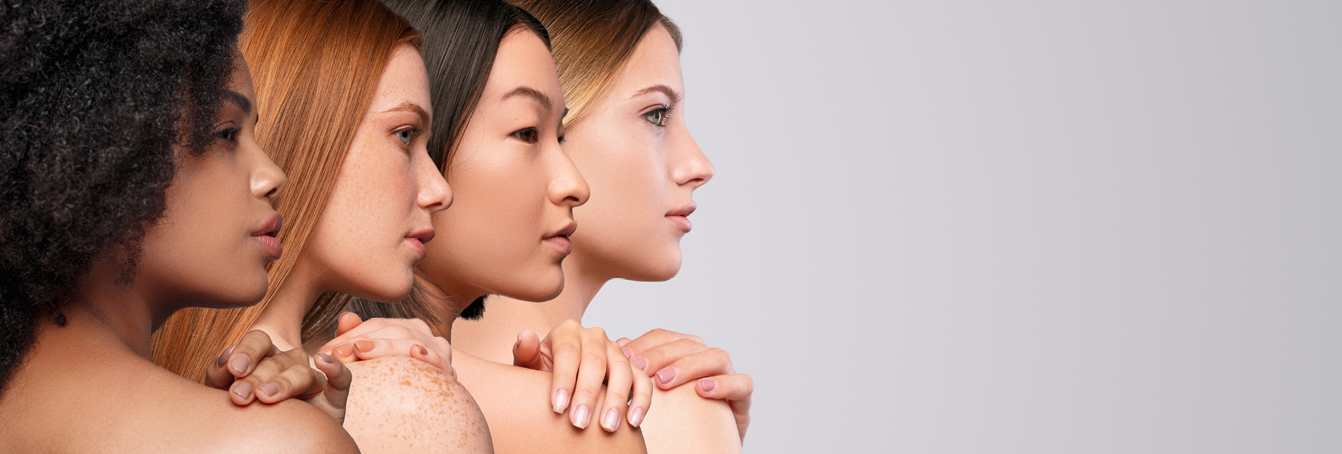 Vier unterschiedliche Frauenköpfe in Reihe von hinten fotografiert schauen sich über die rechte Schulter und fassen sich mit der linken Hand auf die eigene Schulter.